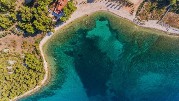 Vue aérienne d’une zone côtière avec des eaux turquoise limpides, une plage de sable et une végétation luxuriante.