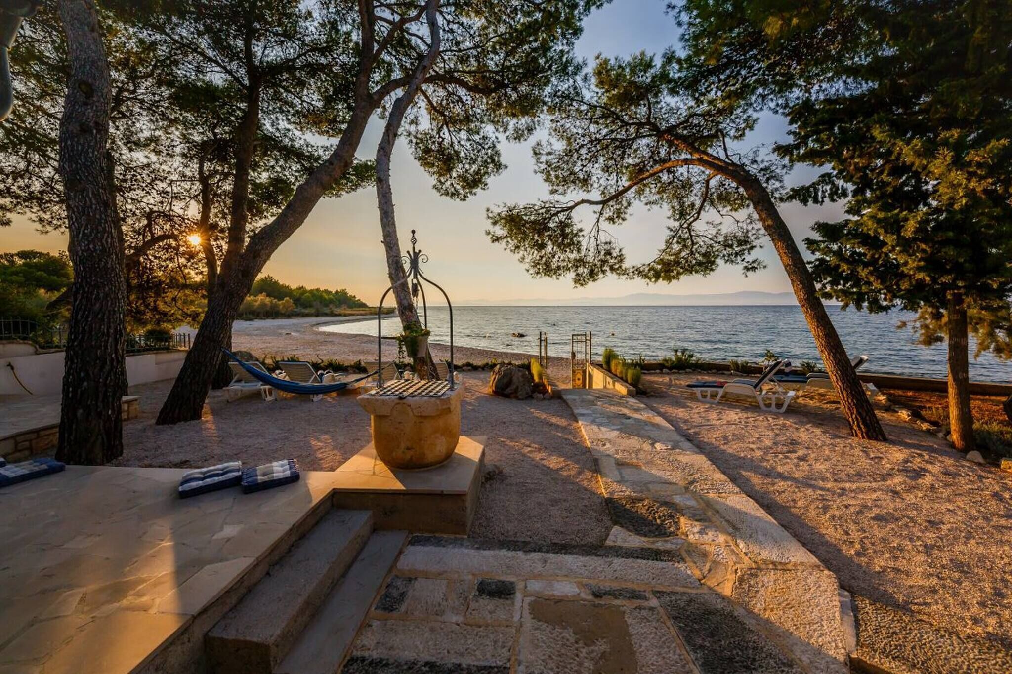 A beachside patio with a stone fire pit, lounge chairs, and a view of the sea.