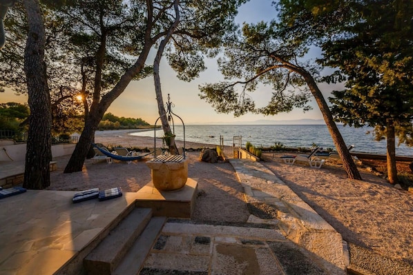 A beachside patio with a stone fire pit, lounge chairs, and a view of the sea.