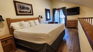 A bedroom with a large bed, a wooden nightstand, a dresser, a TV, and a balcony with curtains. - Newly Renovated ski-in/ski-out condo at Copper Mountain (Frisco)
