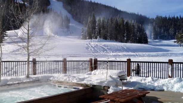 A snowy outdoor area with a wooden deck, a hot tub, and a fenced area. - Newly Renovated ski-in/ski-out condo at Copper Mountain (Frisco)