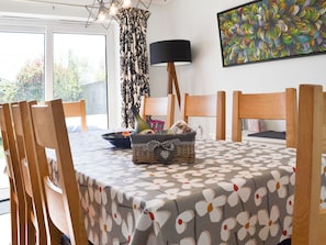 A dining area with a table set for four, a wicker basket with bread, a black lamp, and a colorful abstract painting on the wall. - 4 bedroom accommodation in Sedgeford (Sedgeford)