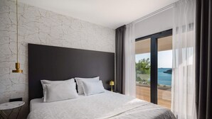 Une chambre avec un grand lit, une petite table, une lampe suspendue et une vue sur la mer.