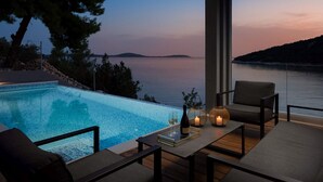 Un espace extérieur moderne, aménagé avec des sièges et une piscine, offrant une vue sur une étendue d’eau et une île lointaine.