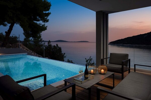A modern outdoor seating area with a pool, overlooking a body of water and a distant island.
