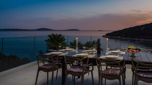 An outdoor dining area with a table set for two, overlooking a body of water and hills.