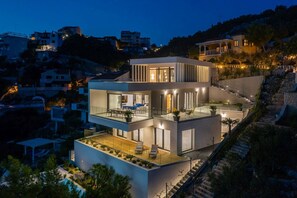 A modern multi-story house with a balcony, a staircase, and a pool area.