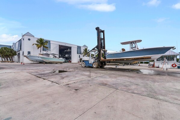 A boat being lifted by a forklift in a marina with a large building in the background.