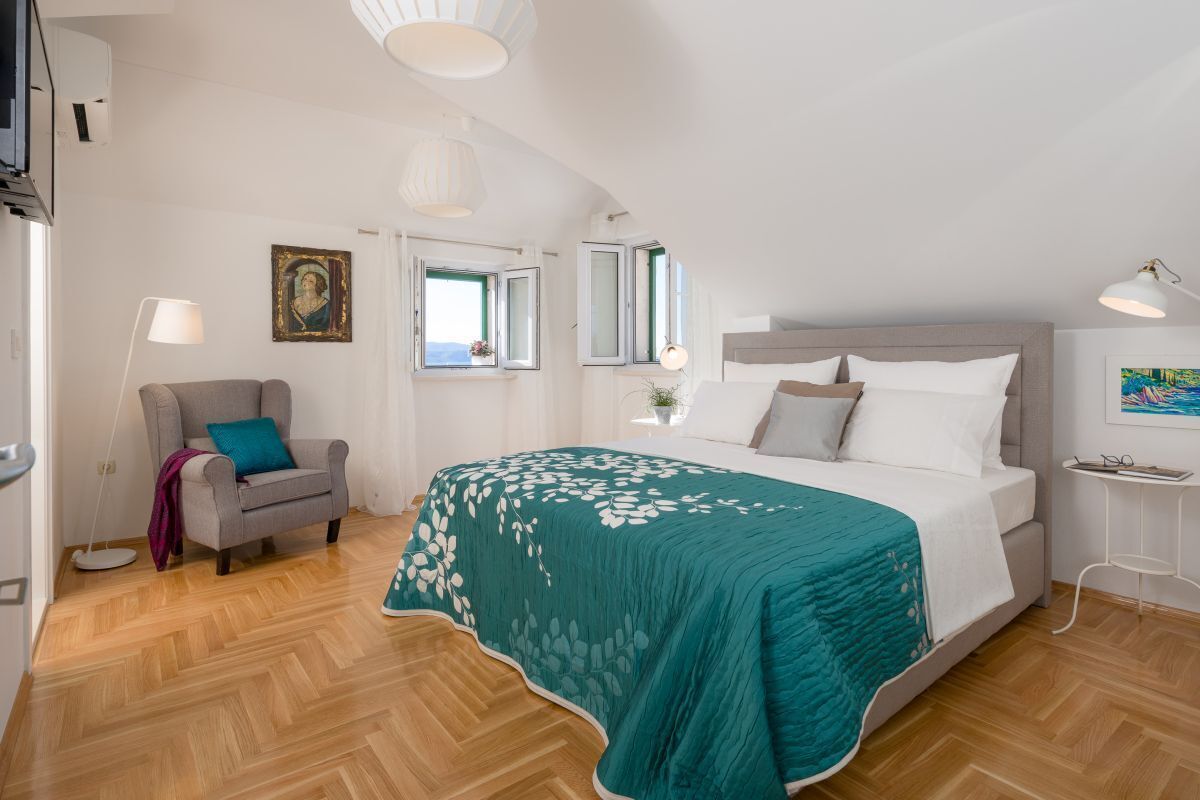 Un dormitorio con cama, una silla, una lámpara y un cuadro en la pared.