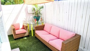 Ein Sitzgarnitur aus Rattan mit passenden Kissen, ein Glastisch und ein Blumentopf.
