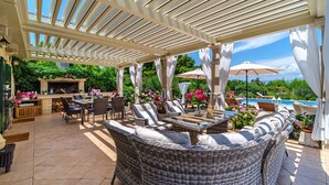 Un patio al aire libre con mobiliario de mimbre, zona de barbacoa y vistas a una piscina.