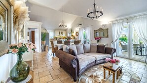 Un salón amplio con un sofá de cuero marrón, una zona de comedor con mesa blanca y una cocina al fondo.