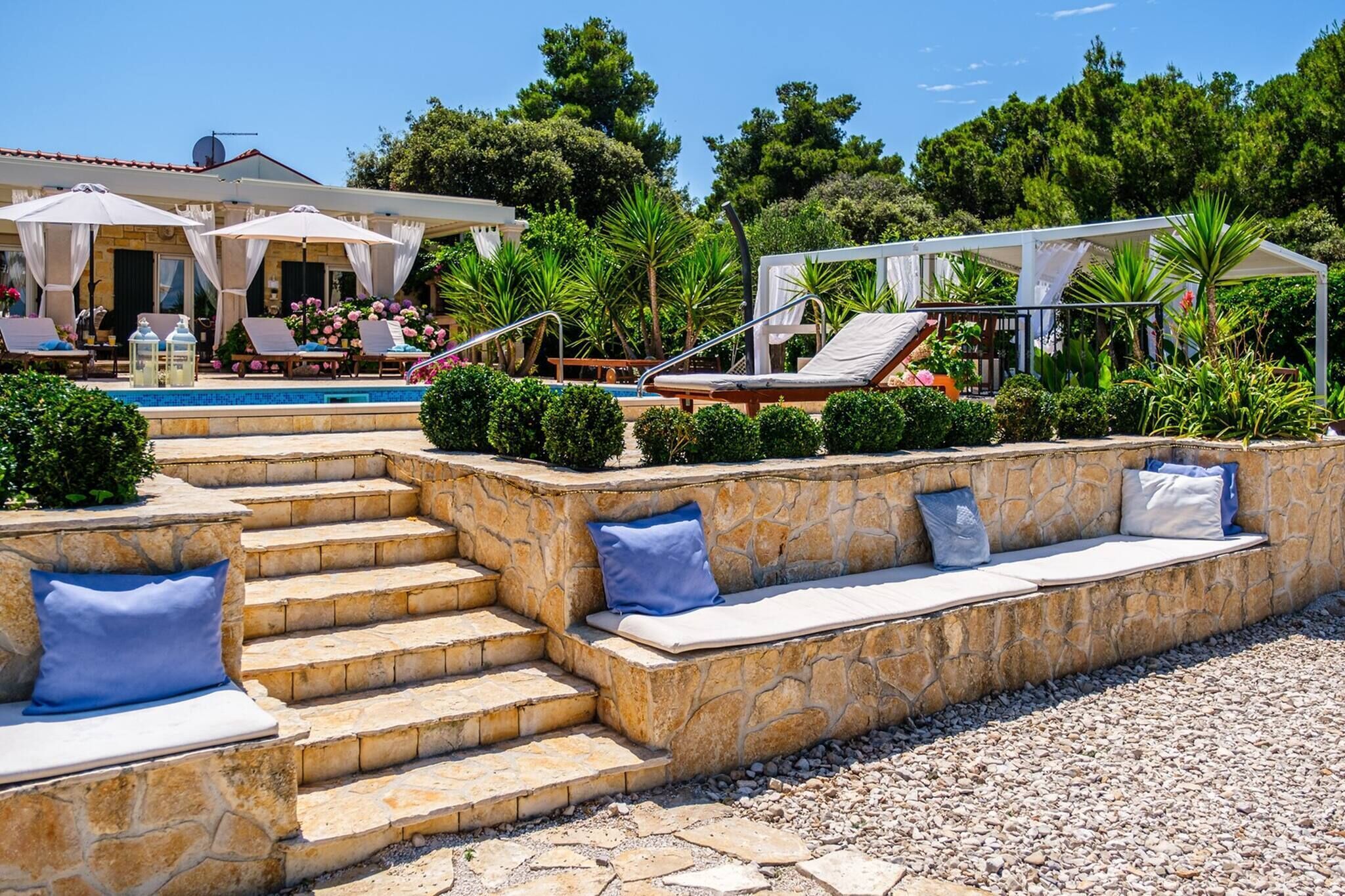 A poolside area with steps leading to a seating area, surrounded by greenery and umbrellas.
