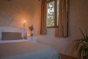 Ein Schlafzimmer mit Bett, Nachttisch, Zimmerpflanze und einem Fenster mit Vorhängen.