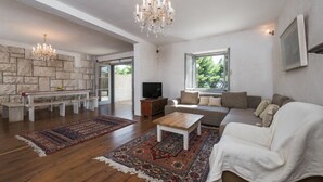 A spacious living room with a stone wall, a chandelier, a sofa, a coffee table, and a television. - Luxury Villa Bol Oasis Brac With Heated Pool (Bol)