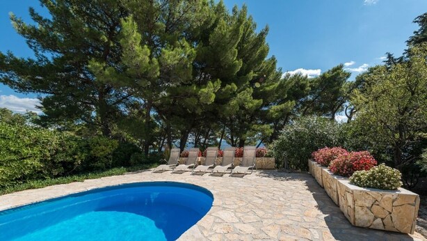 A swimming pool with stone tiles, surrounded by trees and plants. - Luxury Villa Bol Oasis Brac With Heated Pool (Bol)