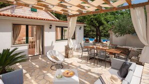 A covered outdoor area with stone flooring, a dining table, chairs, a sofa, and a small table with a plate of fruit.