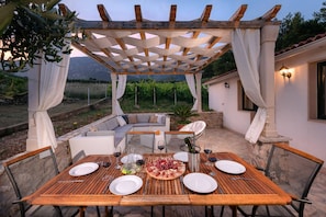 Uma área de refeições ao ar livre com pérgola, assentos e uma mesa posta para uma refeição.