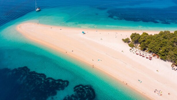 An aerial view of a beach with clear turquoise waters, a sandy shore, and a small boat anchored near the water.