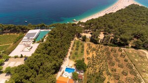 An aerial view of a coastal property with a swimming pool, a beach, and boats in the water.