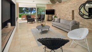 A modern living room with a sofa, coffee table, and chairs, a flat-screen TV mounted on a brick wall, and a large window offering a view of greenery. - Luxury Beachfront Villa Castello Bol with Pool (Bol)