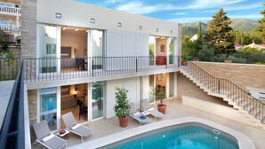 A modern two-story building with a swimming pool, outdoor seating, and a staircase leading to a balcony. - Luxury Beachfront Villa Castello Bol with Pool (Bol)