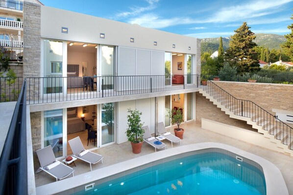 Un bâtiment moderne à deux étages doté d’une piscine, d’un espace extérieur aménagé et d’un escalier menant à un balcon.