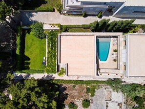 Vue aérienne d’un bâtiment moderne doté d’une piscine, entouré de verdure et situé à proximité d’autres constructions.