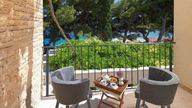A balcony with two chairs, a tray with a teapot, cups, and a vase, and a view of trees and a body of water. - Luxury Beachfront Villa Castello Bol with Pool (Bol)