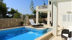 Un espace aménagé au bord de la piscine, avec une piscine à l’eau d’un bleu limpide, des chaises longues et un mur en pierre.