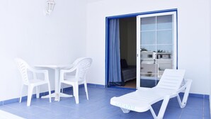 A balcony with a white table and chairs, a white lounge chair, and a blue-framed sliding door leading to a room. - Aguazul (Tías)