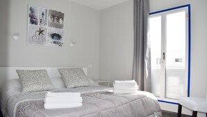 A modern bedroom with a large bed, a side table, a view of the outdoors through a sliding door, and a wall art piece. - Aguazul (Tías)