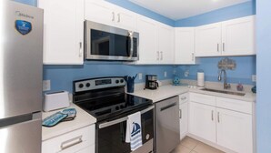 A compact kitchen with white cabinets, a stainless steel refrigerator, a microwave, a stove, and a dishwasher.