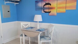 A room with a blue wall, a flat-screen TV, a table with chairs, and a painting of a dolphin.