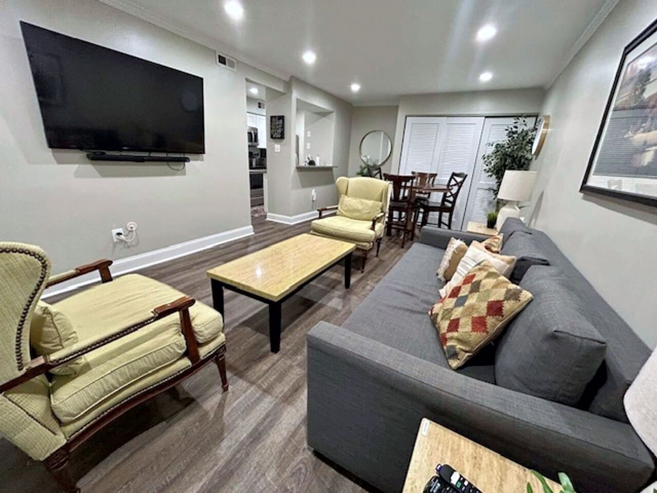 A living room with a flat-screen TV, a grey sofa, a yellow armchair, and a wooden coffee table.