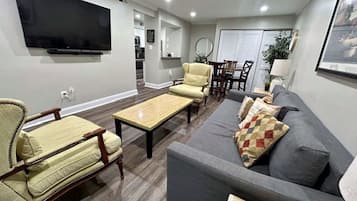 A living room with a flat-screen TV, a grey sofa, a yellow armchair, and a wooden coffee table.