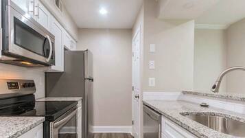A kitchen with a microwave, stove, refrigerator, and granite countertops.