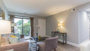 A modern living room with a sofa, a coffee table, and a lamp. There is a sliding glass door leading to a balcony.