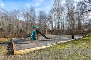 A playground with a slide and climbing structure, surrounded by trees and a clear sky.