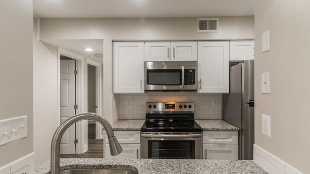 A compact kitchen with white cabinets, a stainless steel microwave, a stove, and a refrigerator.