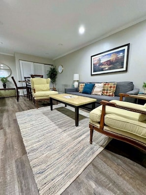 A living room with a sofa, armchairs, a coffee table, a rug, and a painting on the wall.