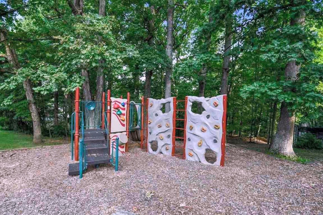 A playground with climbing structures and a slide, surrounded by trees.