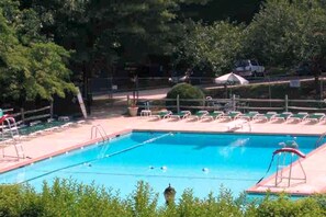 Une piscine dotée de plongeoirs, entourée de chaises longues et de verdure.