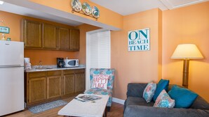 A compact living space with a kitchenette, a sofa, a coffee table, and a chair with a decorative pillow.