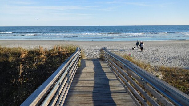 A wooden boardwalk leading to a beach with people walking.