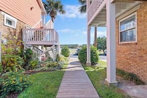 A wooden pathway leading to a building with a balcony and a brick facade.
