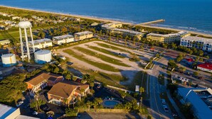 An aerial view of a coastal area with a beach, a pier, and a large water tower.