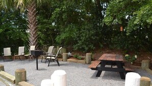 An outdoor seating area with a wooden table and chairs, surrounded by trees and gravel. - Beachy Isle of Palms Studio! Close walk to BEACH! (Isle of Palms)