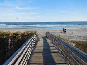 Une promenade en bois qui mène à une plage où l’on voit des gens se promener.