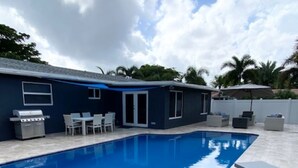 A swimming pool with lounge chairs, a barbecue grill, and a covered patio area.